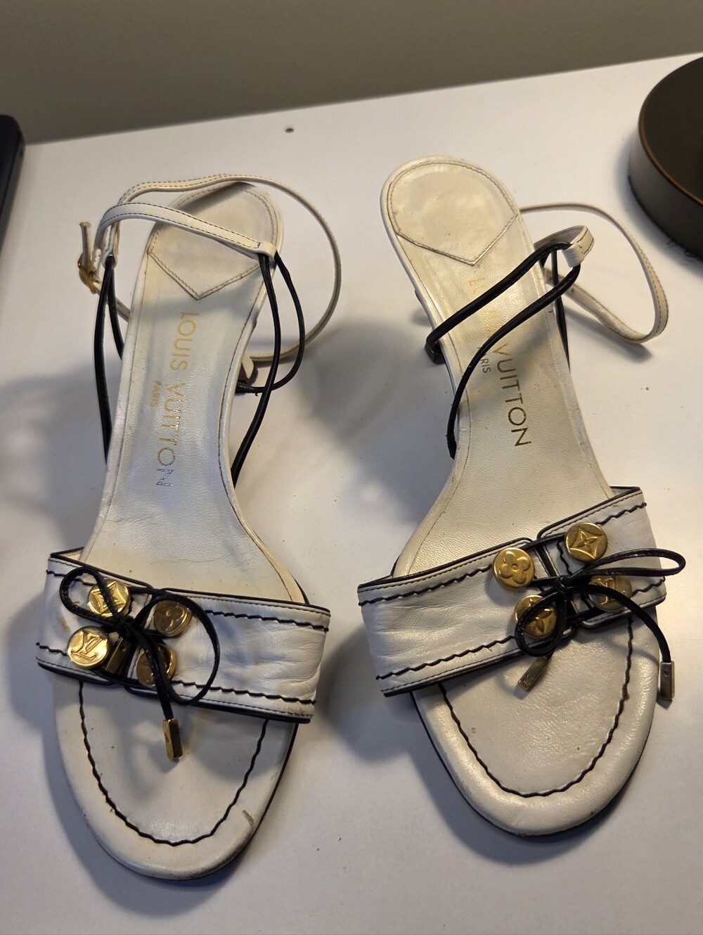 Louis Vuitton white leather sandals feature black ankle straps gold-toned floral